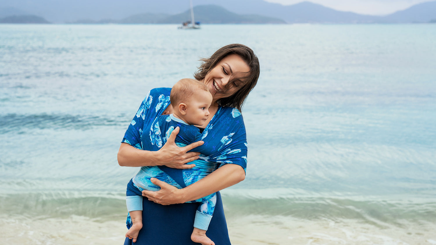Mother carries an infant in IVAU baby wrap by the seaside